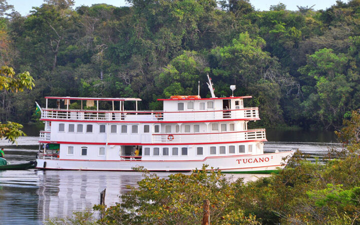 Tucano Amazon ship seen on its starboard side amid green trees in the foreground and background