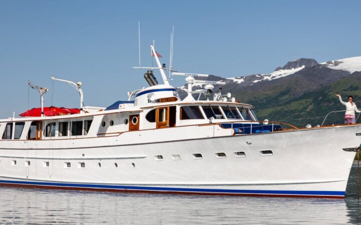 Small white yacht Sea Star idles in glassy water beneath a green & white hillside during the AK Explorer Kenai & Prince William Sound tour.