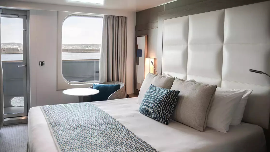 stateroom aboard L'Austral expedition ship, showing king bed, desk & white-&-copper appointments.