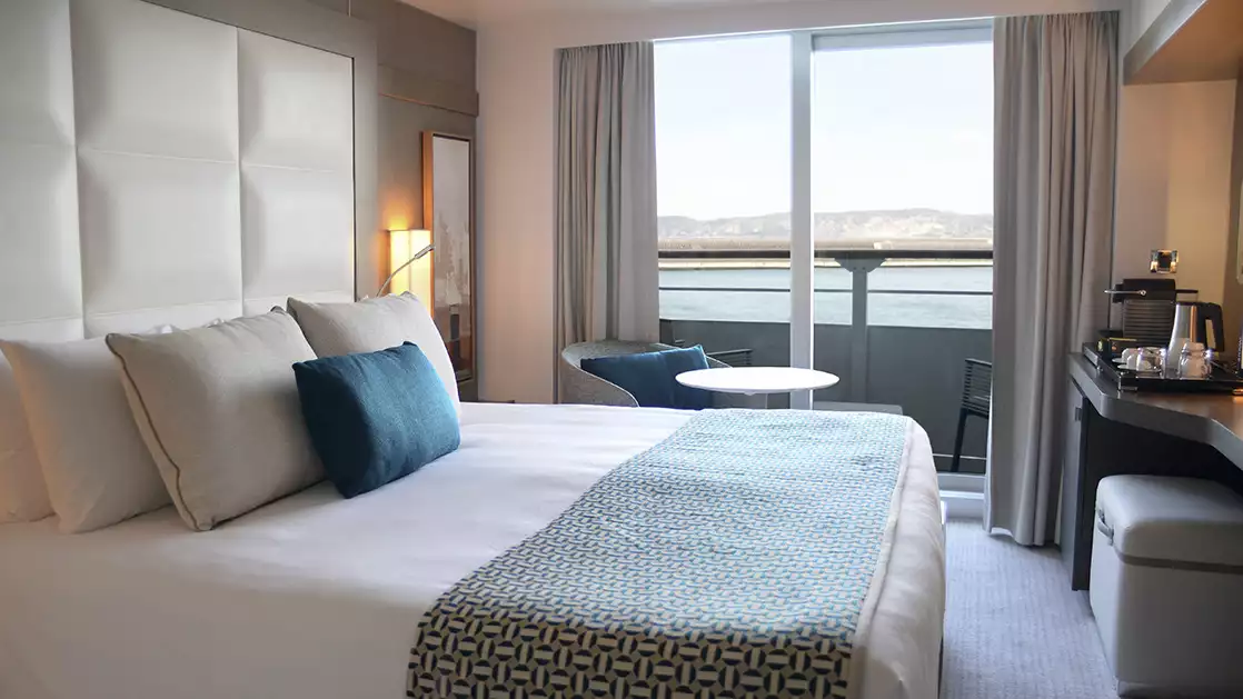 prestige stateroom aboard L'Austral expedition ship, showing king bed, table, chair & white-&-copper appointments.