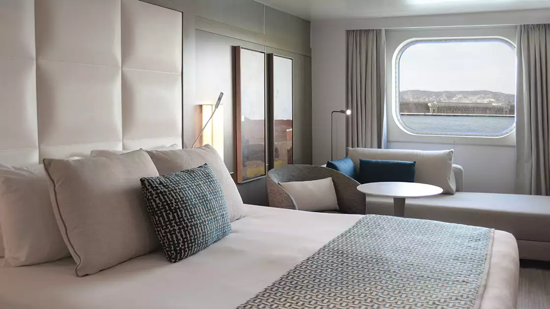 Superior stateroom aboard L'Austral expedition ship, showing king bed, desk, lamp & white-&-copper appointments.