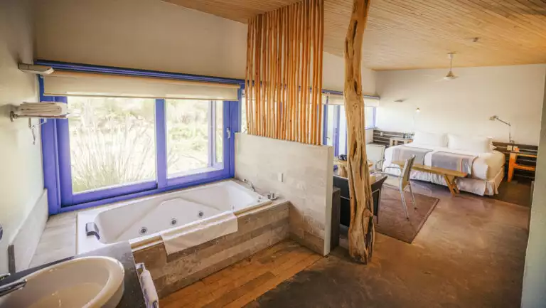 Large room of Catur Suite with bed, loveseat, table & chairs, jetted bathtub & large windows at Explora Atacama Lodge in Chile.