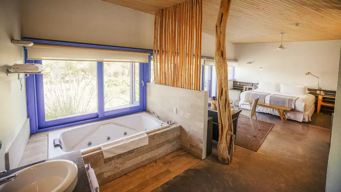 Large room of Catur Suite with bed, loveseat, table & chairs, jetted bathtub & large windows at Explora Atacama Lodge in Chile.