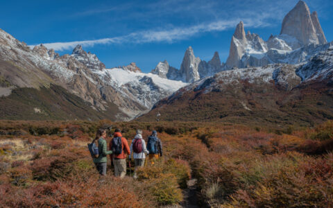 Explora El Chalten guests walk through autumnal valley under a blue sky en route to tall jagged peaks in the distance.