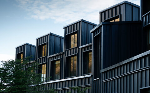 Dark steely exterior of a modern lodge with tall windows sitting beside a tree on the Explora El Chaltén trip.