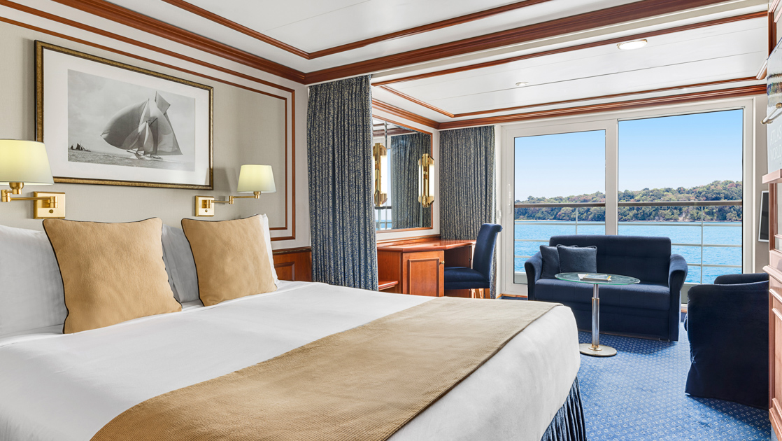 Category 5 cabin on Nat Geo Orion ship with double bed in white & beige, curtain to seating area & shared balcony.