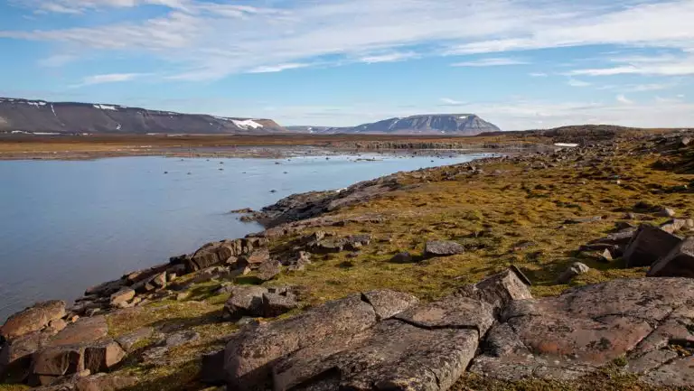 Inlet with glassy water, mossy rocks & blue sky, seen on the South Spitsbergen Explorer cruise in the Arctic.