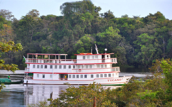Tucano Amazon ship seen on its starboard side amid green trees in the foreground and background