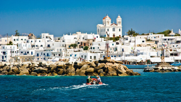 Red Zodiac with Greece & Turkey cruise guests makes its way towards small harbor of whitewashed hillside town in Greece.