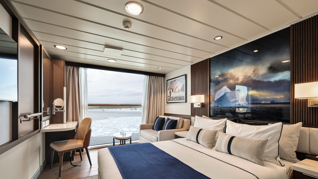 Superior Stateroom on Douglas Mawson ship with king bed in white linens, dark wood walls, full-size view window & wildlife photo.