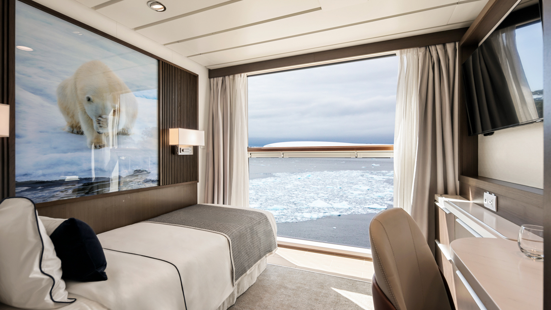 Superior Single Stateroom on Douglas Mawson ship with twin bed in white linens, dark wood walls, porthole & wildlife photos.