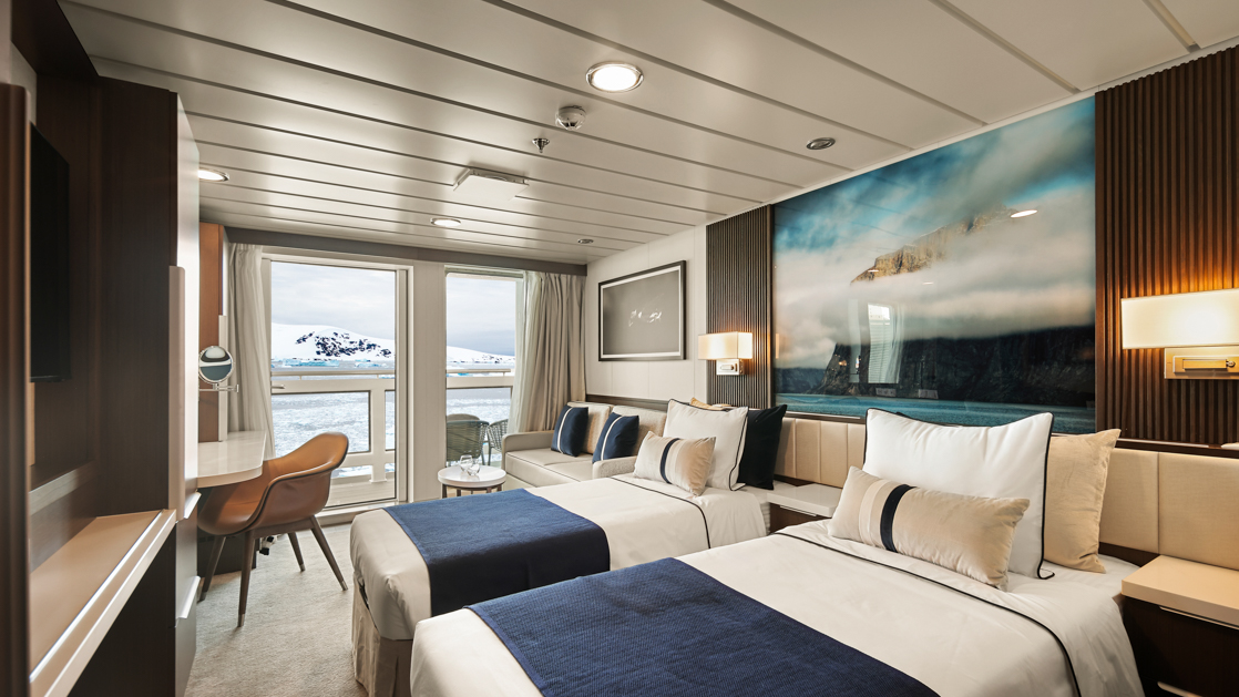 Category A Balcony Stateroom on Douglas Mawson ship with king bed in white linens, dark wood walls, balcony & wildlife photo.