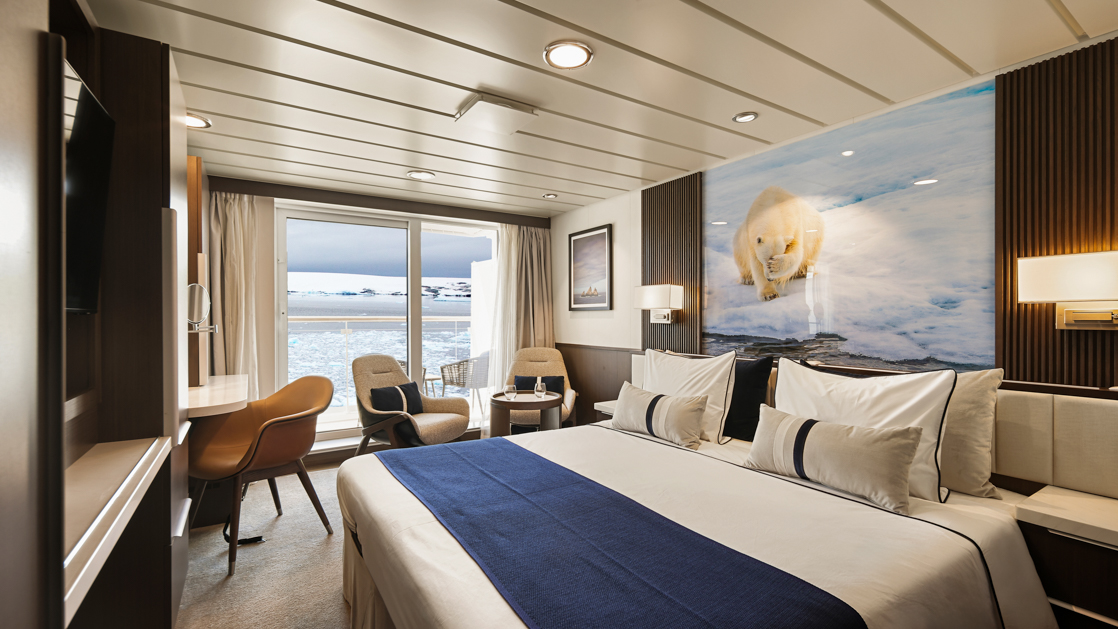 Category C Balcony Stateroom on Douglas Mawson ship with king bed in white linens, dark wood walls, balcony & wildlife photo.