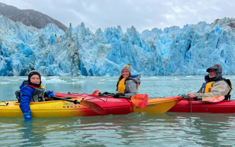 three Kayakers posing infront of the blue and white icebergs of alaska