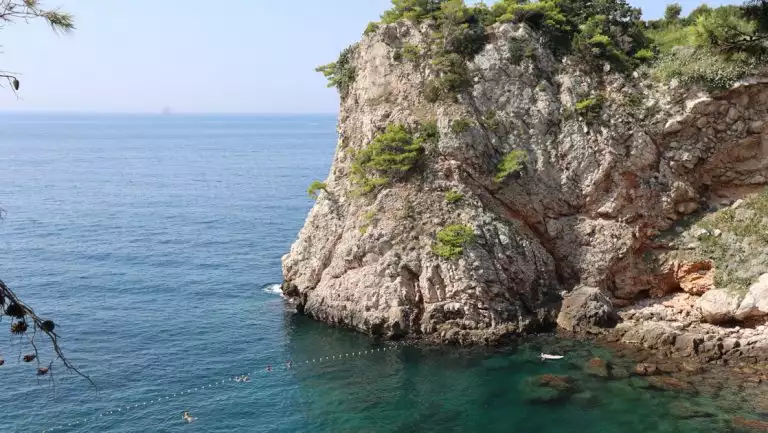 Small inlet of turquoise water by tall beige cliffs with green shrubs, seen on a small ship cruise to Croatia, Albania & Greece.