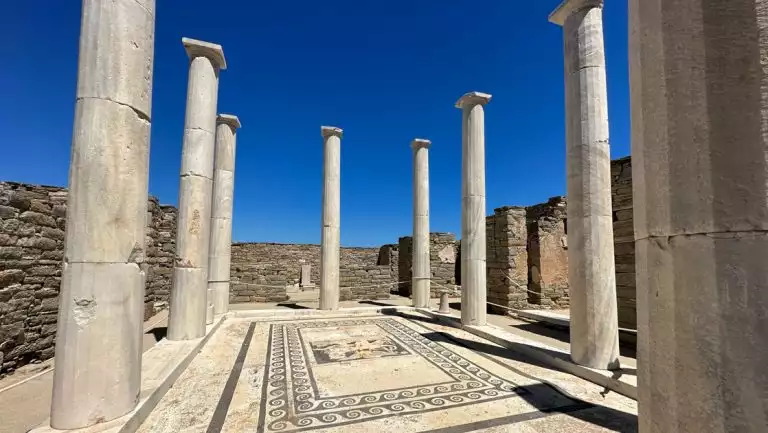 Beige Greco-Roman stone columns surround an open-air pavilion with marble patterns inlaid, seen on a Greece and Turkey cruise.