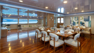Dining area of Petrel catamaran in Galapagos with wood floor, 2 8-guest tables, dark wood chairs & marble food servicebar.