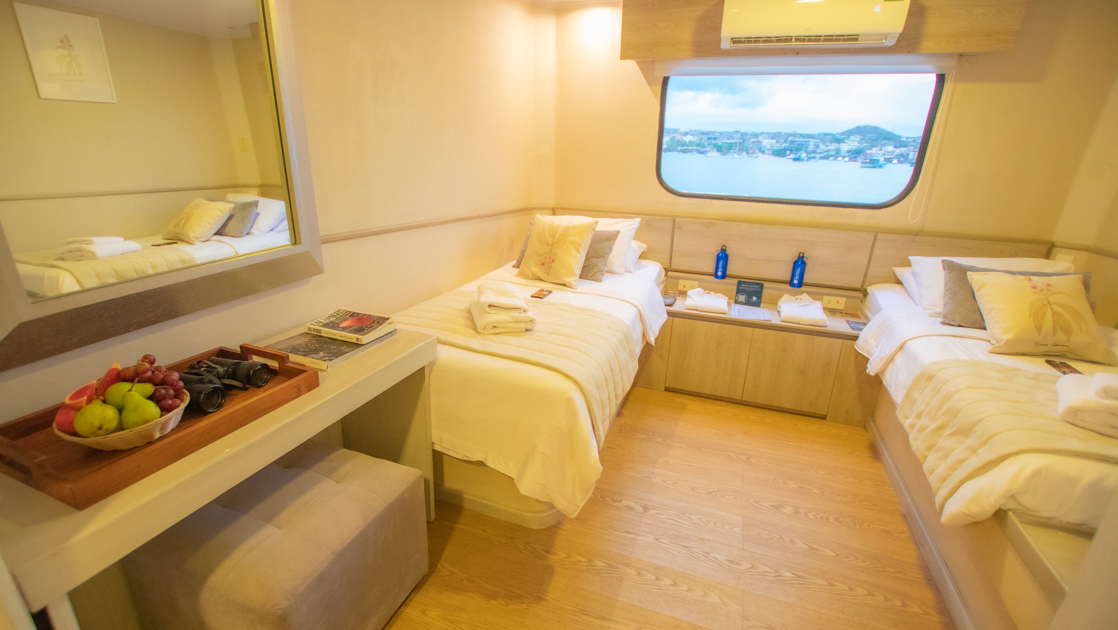 2 twin beds in a light and airy suite with natural wood tones and bedding aboard the Seaman Journey in the Galapagos