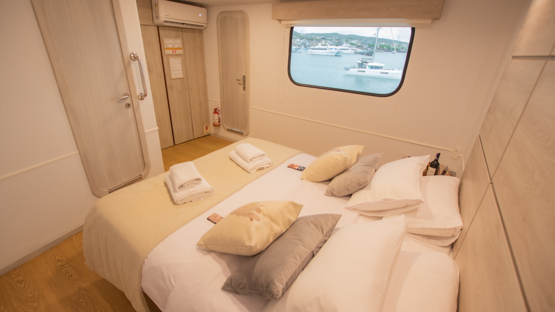 A large bed within a light and airy suite with natural wood tones and bedding aboard the Seaman Journey in the Galapagos
