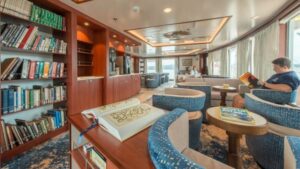 Man reads in armchair beside large window in library aboard National Geographic Endeavour II expedition ship in the Galapagos Islands