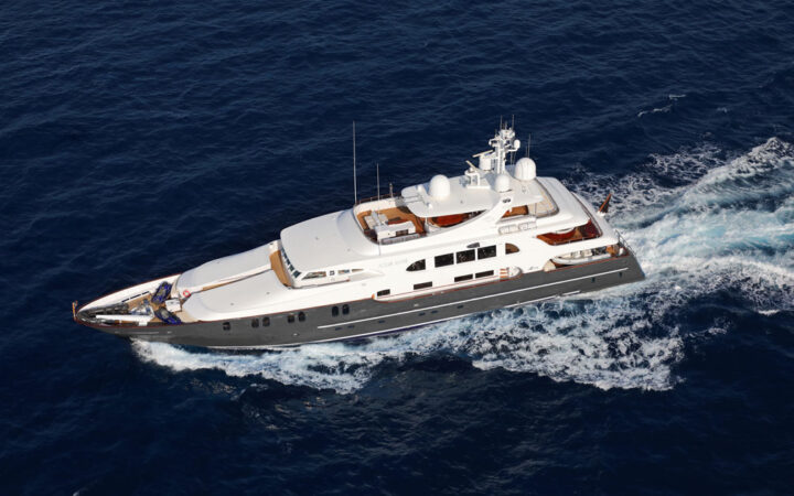 Aerial view of superyacht in Galapagos Aqua Mare cruising at speed in calm water, with blue hull, teak decks & white upper decks.