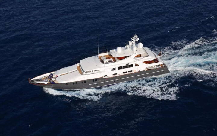 Aerial view of superyacht in Galapagos Aqua Mare cruising at speed in calm water, with blue hull, teak decks & white upper decks.