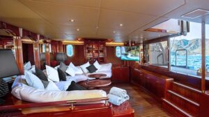 Covered Beachclub lounge area on Aqua Mare Galapagos superyacht, with partial open-air view, large white sofa & veneer everything.