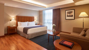 Presidential Suite at Hotel Oro Verde with double bed in white sheets, wood floor, couch & floor-to-ceiling window.