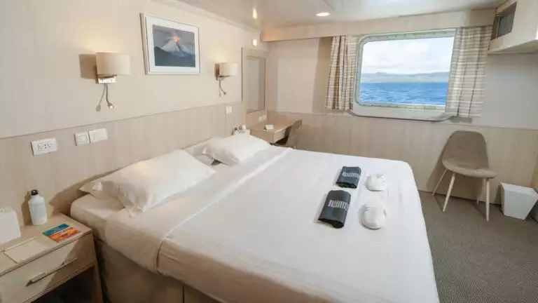 Isabela II Owners Cabin with double bed, nightstand, window, small table and chairs.