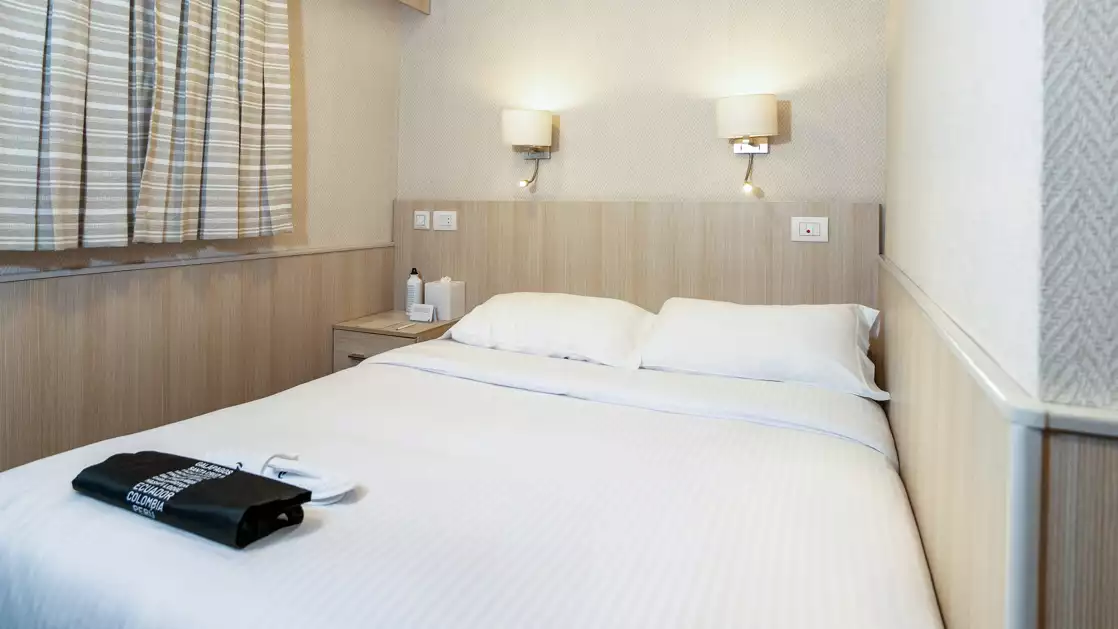 Isabela II stateroom with double bed, chairs, nightstands and reading lights.