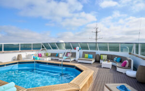 Sun Deck on Nat Geo Islander II ship in Galapagos with large Jacuzzi & many gray chaise loungers with colored throw pillows.