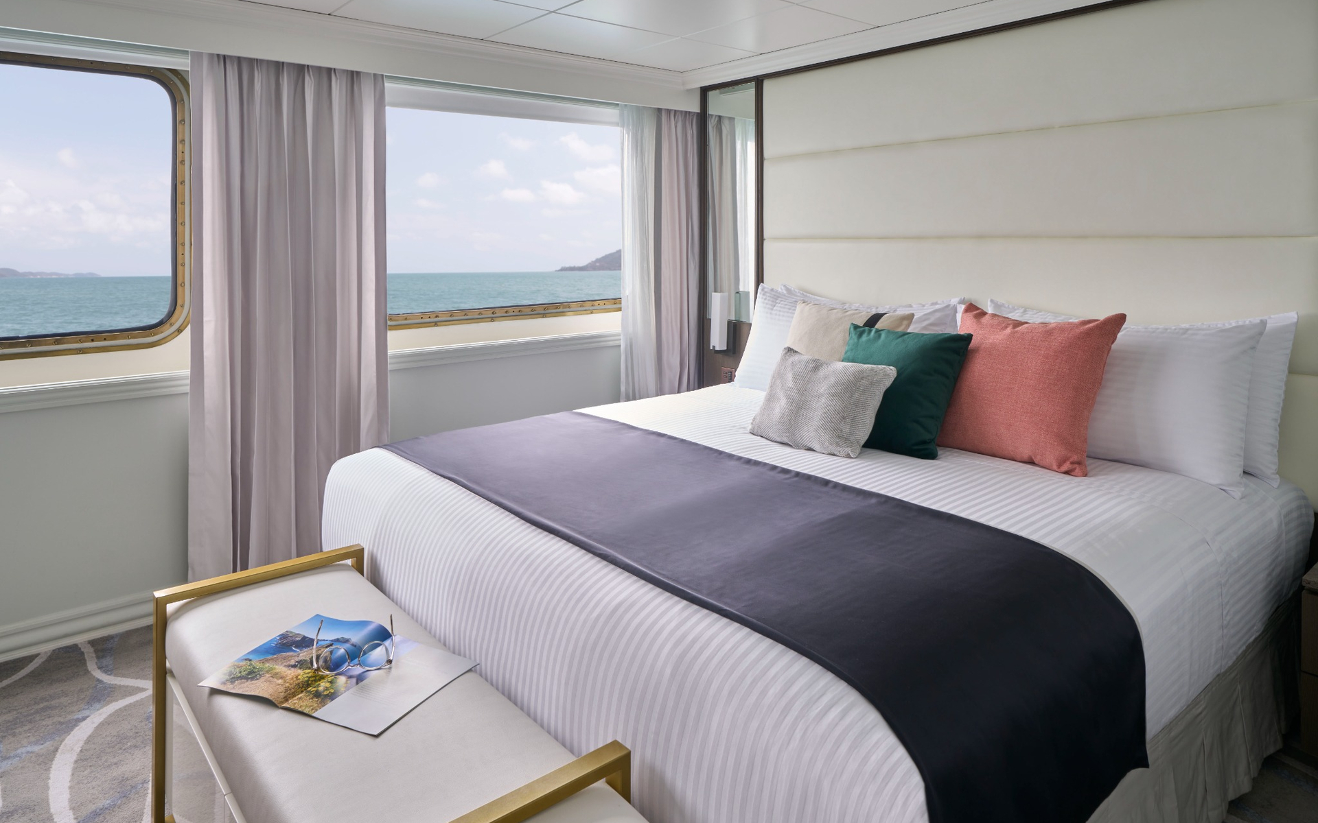 Suite aboard National Geographic Islander II Galapagos ship with double bed, large view windows & white & blue decor.