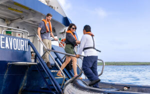 Woman holds hand of crew member while stepping from Nat Geo Endeavour II ship onto a Zodiac boat in Galapagos