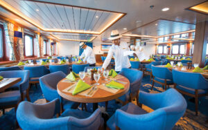 Crew members set the tables in the dining room awash with natural light aboard National Geographic Endeavour II expedition ship in the Galapagos Islands