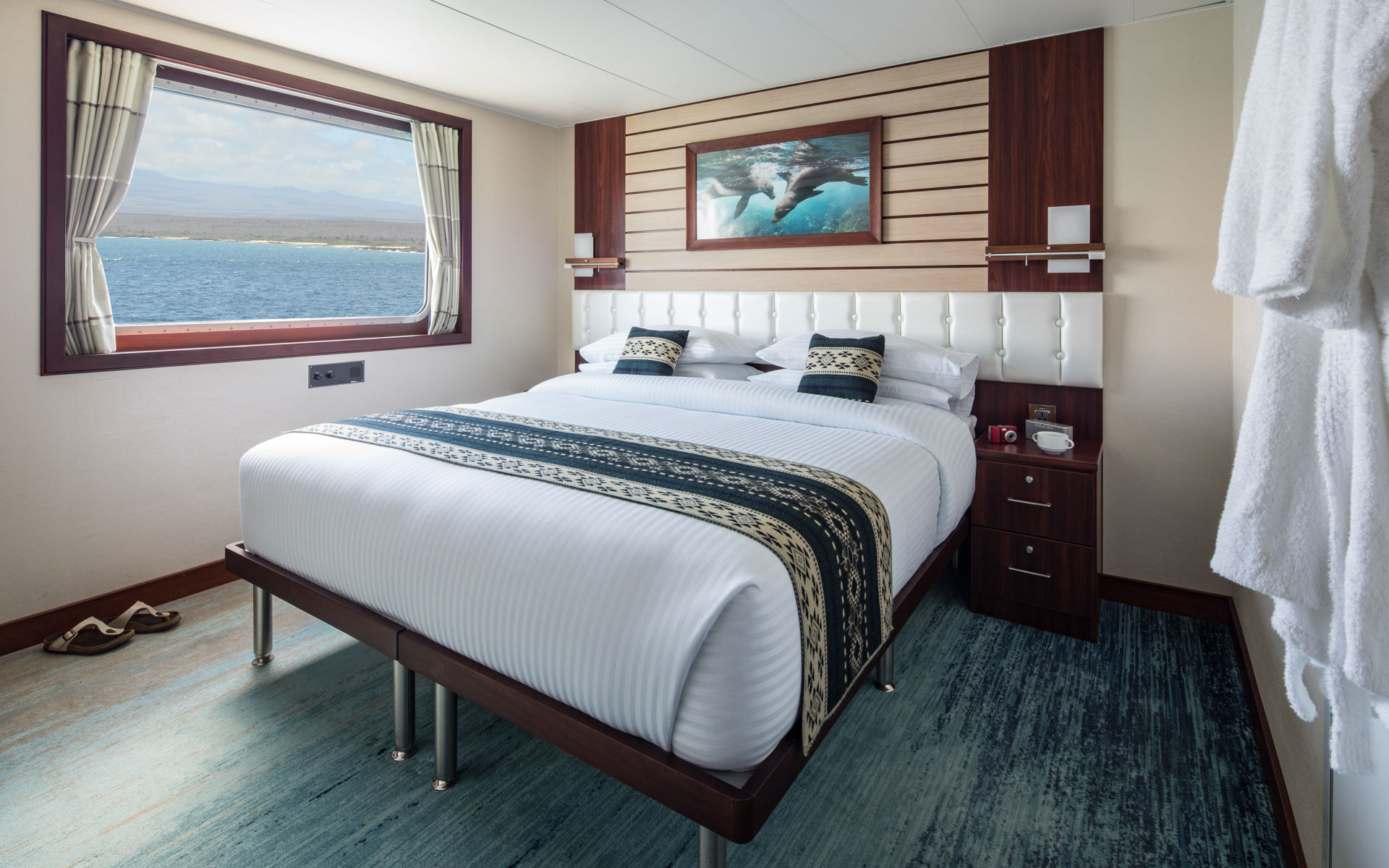 Cabin with large bed beside large picture window aboard Cabin with large bed, armchair, large window aboard National Geographic Endeavour II in the Galapagos Islands