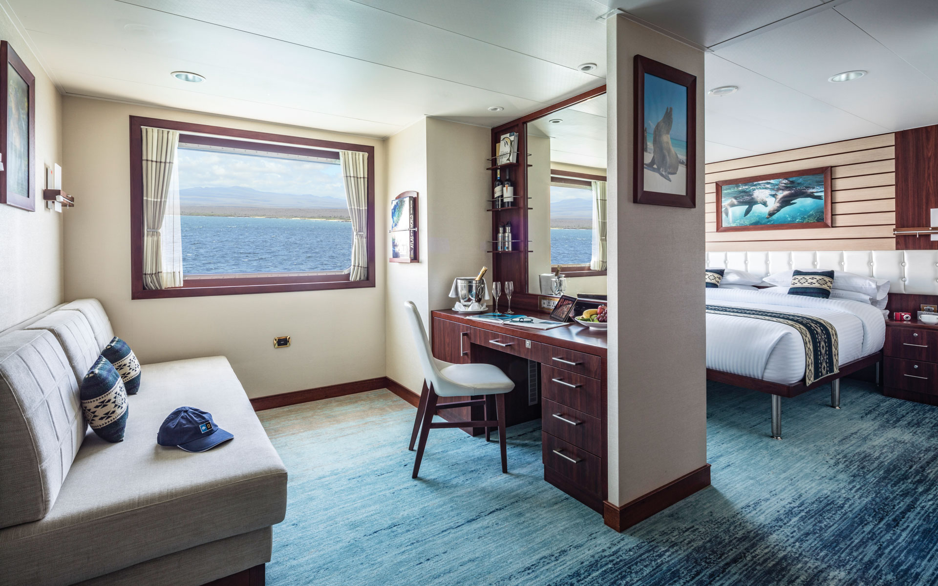 Suite C interior with large bed, couch, desk, chair and large windows aboard National Geographic Endeavour II expedition ship in the Galapagos Islands
