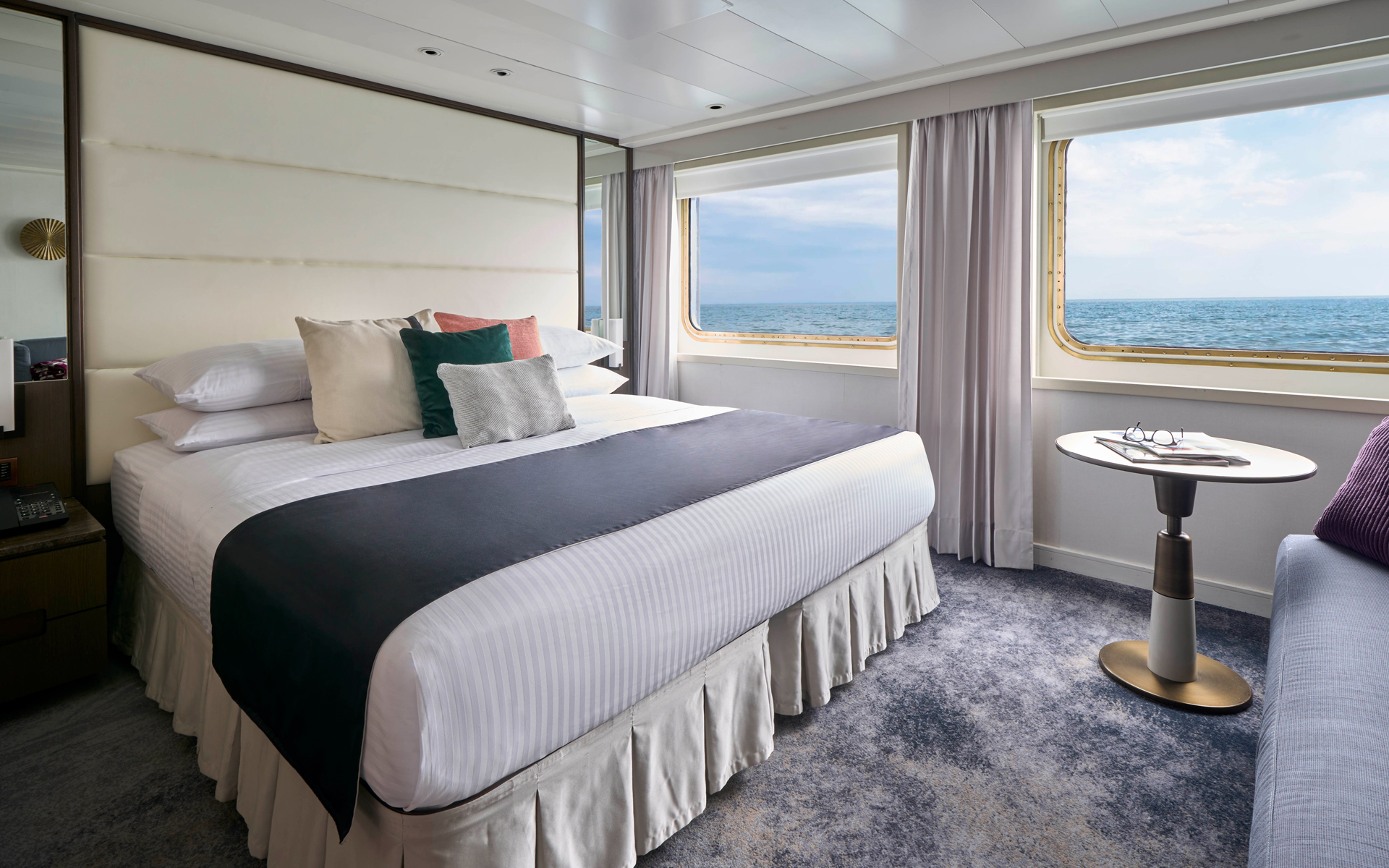 Suite aboard National Geographic Islander II Galapagos ship with double bed, large view windows & white & blue decor.