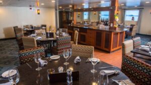 Safari Voyager Costa Rica small ship dining room with tables and chairs throughout and a bar in the background