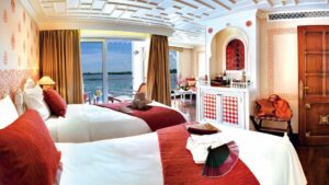 Category 1 stateroom with twin beds, large windows, dresser and lots of red accents