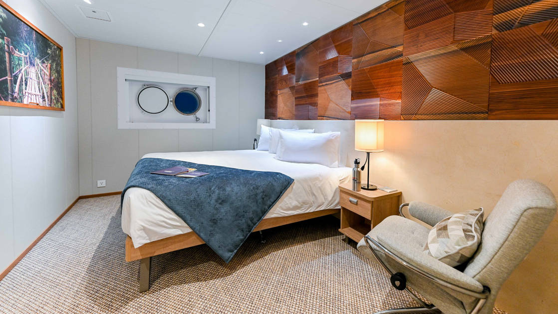 Coral Deck Stateroom aboard Coral Adventurer with bed, chair, and porthole.