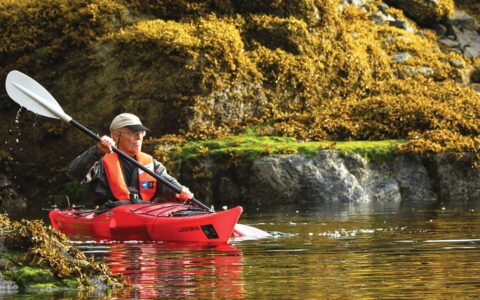 a traveler in a red kayak paddles through still waters in the san juan islands in the pacific northwest on a sunny day
