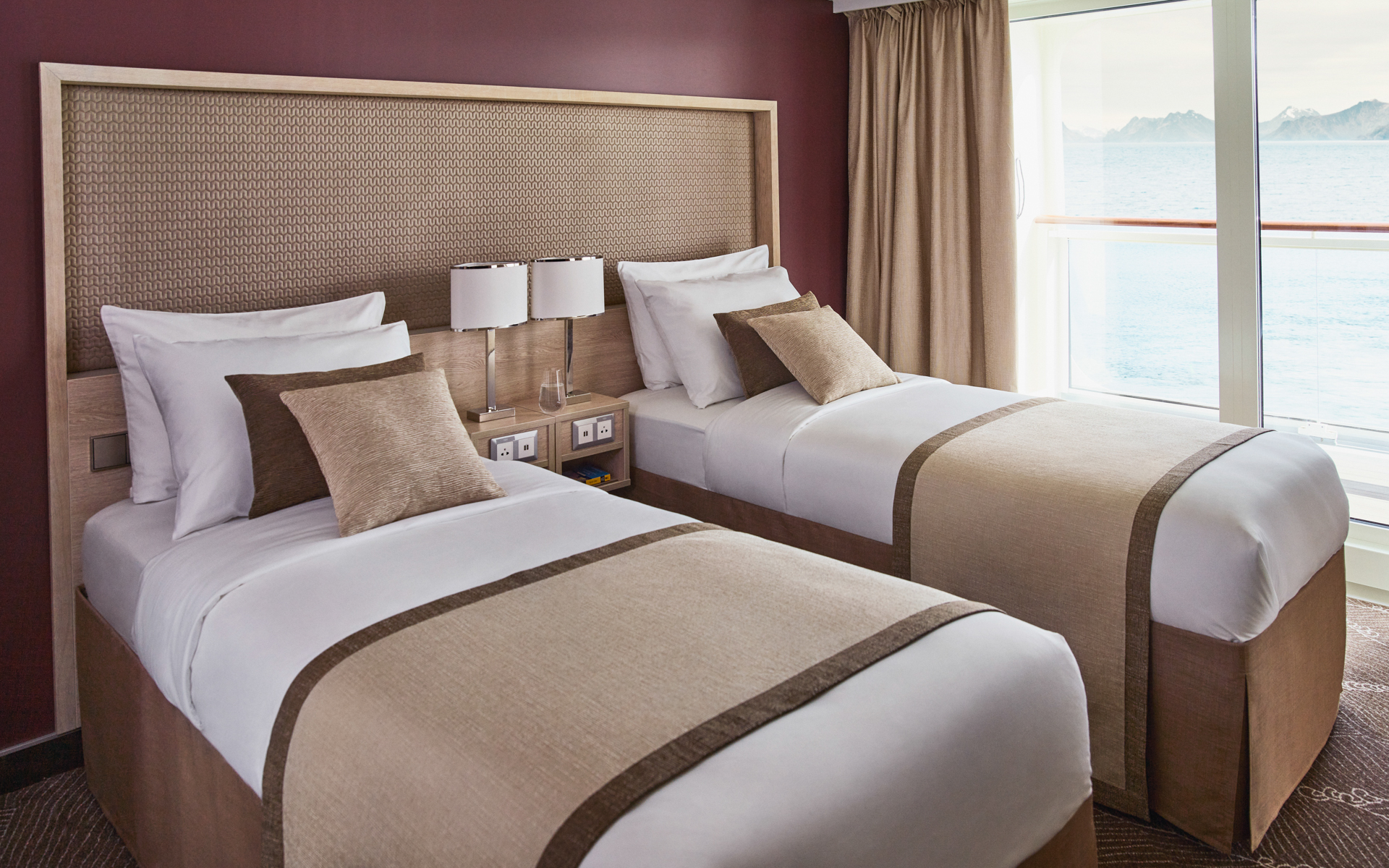 Two single beds with a shared nightstand and individual reading lights. The white duvets are accented with cream and brown.