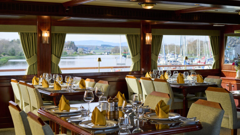 Lord of the Glens dining room with table and chairs, set up for a meal with large picture windows and wood paneling.