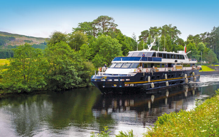 Small ship Lord of the Glens cruising past the Urquhart Castle in the Loch Ness highlands of Scotland