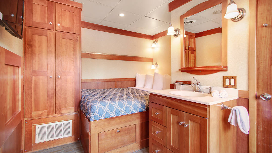 Navigator stateroom with a large bed, nightstand and dresser aboard the Safari Explorer Hawaii small ship