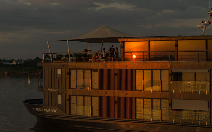 Aqua Mekong ship cruising on calm waters with a sunset reflection.