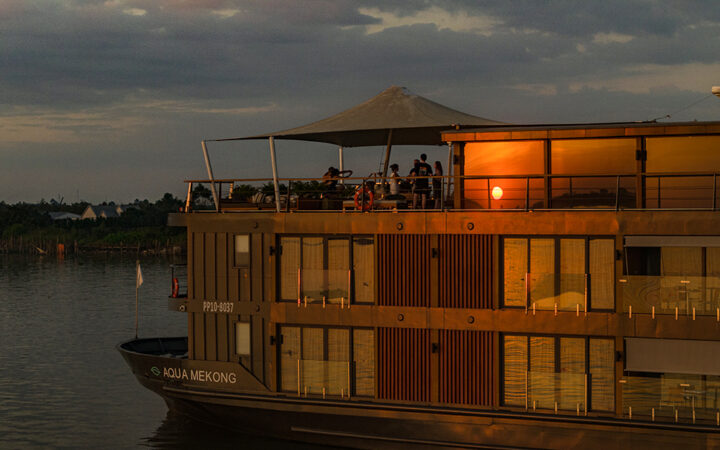 Aqua Mekong ship cruising on calm waters with a sunset reflection.