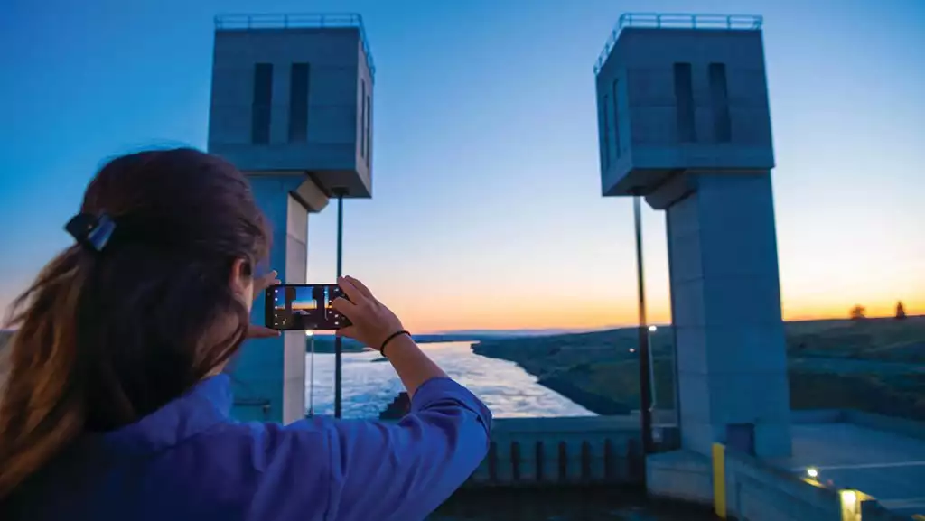 Women taking iphone image of sunset over a dam