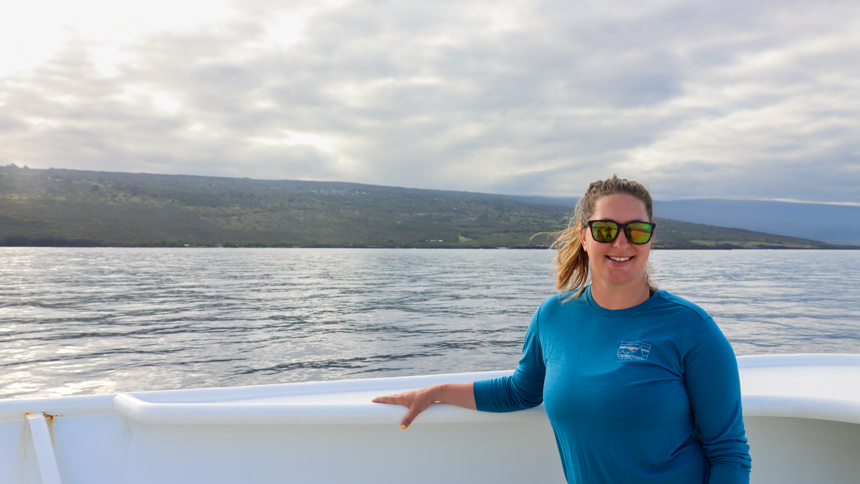 Adventuresmith Taylor standing on the edge of the balcony aboard safari explorer in Hawaii on a gloomy day with a blue shirt and sunglasses