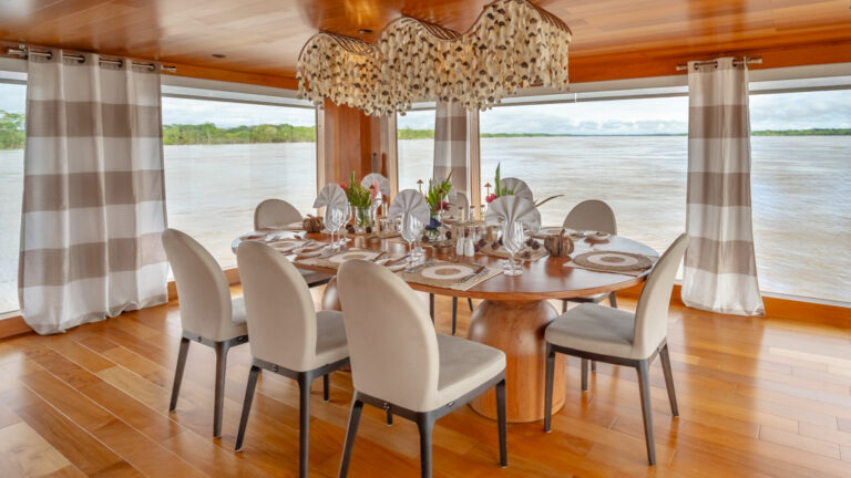 Dining room aboard a small ship cruise with an upscale space setting, with grand floor-to-ceiling windows